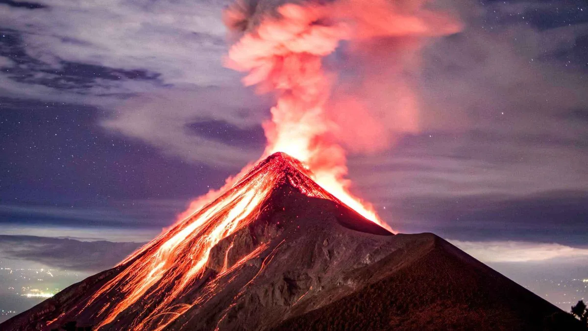 Volcan de Fuego erupting with glowing lava streaming down its cone at night, seen from an Acatenango volcano tour campsite near Antigua, Guatemala