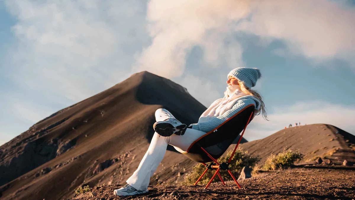 Hiker resting on volcanic sand below a steaming crater on a private overnight Acatenango volcano tour near Antigua, Guatemala